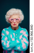 A humorous portrait of a grumpy elderly woman with vibrant pink glasses and a fluffy turquoise and pink sweater, arms crossed, conveying disapproval, perfect for character study. Стоковое AI-изображение, AI-художник Данила Большаков / Фотобанк Лори