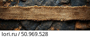 Close-up of a textured brown burlap ribbon laid horizontally across a dark, rugged stone background, highlighting the rustic contrast between natural materials and rough surfaces. Стоковое AI-изображение, AI-художник Данила Большаков / Фотобанк Лори