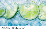 Vibrant green lime citrus slices and clear ice cubes immersed in effervescent, crystal-clear carbonated water with abundant bubbles, creating a cool and refreshing beverage background. Стоковое AI-изображение, AI-художник Данила Большаков / Фотобанк Лори