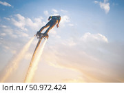 A flyboard athlete hovers over the water against the sunset sky, propelled by powerful jet streams of water. Flyboarding adventure at sunset over calm waters showcasing an exhilarating water sport. Стоковое фото, фотограф Владимир Разгуляев / Фотобанк Лори