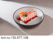 Cheesecake slice with graham crust, strawberry syrup, mint leaf and edible flower served on a modern ceramic plate in soft natural light. Стоковое фото, фотограф Aleksandr Gavrilychev / Фотобанк Лори