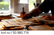 A person is seated at a table surrounded by an assortment of papers and documents. Стоковое AI-изображение, AI-художник Данила Большаков / Фотобанк Лори