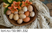 A rustic still life featuring speckled and brown eggs nestled in a wooden bowl, adorned with vibrant orange lilies and a soft cream-colored knitted textile. Стоковое AI-изображение, AI-художник Данила Большаков / Фотобанк Лори