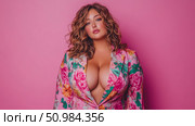 Confident woman with wavy hair posing in a vibrant pink floral blazer, exuding allure against a solid studio background. Стоковое AI-изображение, AI-художник Данила Большаков / Фотобанк Лори
