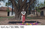 Tribal spiritual leader wearing traditional body paint, conducting sacred ritual near decorated tree, holding ritualistic objects, surrounded by village offerings in rural landscape. Стоковое AI-видео, аниматор Данил Руденко / Фотобанк Лори