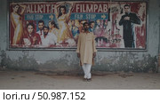 Traditional clothed Pakistani male posing beside faded Bollywood poster, highlighting cultural complexity and urban textures in Pakistan. Стоковое AI-видео, аниматор Данил Руденко / Фотобанк Лори