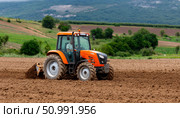 Farmer driving orange tractor plowing cultivated field in countryside. Стоковое фото, фотограф Юрий Поздников / Фотобанк Лори