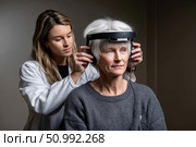 Doctor placing headphones with sensors on patient's head for neurofeedback therapy. Стоковое фото, фотограф Юрий Поздников / Фотобанк Лори