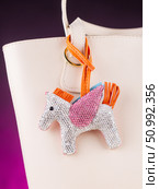 Close-up of an elegant bag charm featuring a Pegasus-shaped pendant encrusted entirely with sparkling rhinestones on white  bag. Стоковое фото, фотограф Виталий Сова / Фотобанк Лори