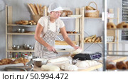 Professional young female baker in white uniform carefully slicing and weighting dough on flour-covered worktable in cozy bakery filled with freshly baked bread and baking tools. Стоковое видео, видеограф Яков Филимонов / Фотобанк Лори