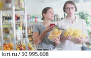 Couple scans the QR code on crispy snacks and potato chips , reads information about the composition. Woman scans the barcode and helps husband make an online payment. Стоковое видео, видеограф Яков Филимонов / Фотобанк Лори