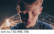 Young Caucasian child wearing face paint, standing inside chalk magic circle, flanked by burning candles, evoking mystical ritualistic environment. Стоковое AI-видео, аниматор Данил Руденко / Фотобанк Лори