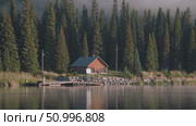 Wooden cabin mirroring calm lake surface, positioned near pine forest edge, small wooden pier extending into tranquil water landscape. Стоковое AI-видео, аниматор Данил Руденко / Фотобанк Лори