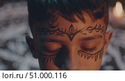 Young child meditating, wearing ceremonial face paint, closed eyes near illuminated candle with ritual white ground markings. Стоковое AI-видео, аниматор Данил Руденко / Фотобанк Лори