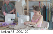 Young dressmaker works on a sewing machine against the background of a mature worker who checks a sample of a dress on a mannequin. Dressmakers work in the sewing industry. Стоковое видео, видеограф Яков Филимонов / Фотобанк Лори