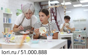 Experienced mature female ceramicist teaching young enthusiastic girl art of ceramic glazing and painting in pottery studio. Стоковое видео, видеограф Яков Филимонов / Фотобанк Лори