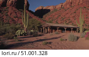 Weathered wooden cabin standing among towering cacti, surrounded by iconic red rock formations of Arizona desert landscape under pristine blue sky. Стоковое AI-видео, аниматор Данил Руденко / Фотобанк Лори
