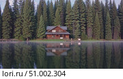 Wooden cabin reflecting in still lake, surrounding pine trees mirroring peaceful morning stillness in wilderness landscape. Стоковое AI-видео, аниматор Данил Руденко / Фотобанк Лори