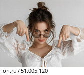 Девушка в белой блузе с очками указывает вниз на светлом фоне. Стоковое AI-изображение, AI-художник Владимир Трубицын / Фотобанк Лори
