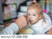 A caring man with a beard feeds his little daughter. A little girl sits at a children's dining table and dines with her dad. Happy fatherhood. Стоковое фото, фотограф Михаил Решетников / Фотобанк Лори