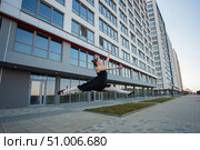 Ballerina in tutu posing against a residential building. Beautiful young woman in black dress and pointe shoes jumping with incredible flexibility. Ballerina performs elegant jumping with deflection. Стоковое фото, фотограф Михаил Решетников / Фотобанк Лори