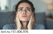 A young woman expresses frustration, covering her ears in distress while seated in a cozy living room during the late afternoon hours. Стоковое AI-видео, аниматор Данила Большаков / Фотобанк Лори