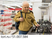 elderly grayhaired man pensioner looking gas hob at counter in showroom of electrical appliance hypermarket department. Стоковое фото, фотограф Татьяна Яцевич / Фотобанк Лори