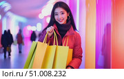 A young woman enjoys a night out shopping, holding bright yellow bags in a lively, illuminated environment filled with colorful lights. Стоковое AI-видео, аниматор Данила Большаков / Фотобанк Лори