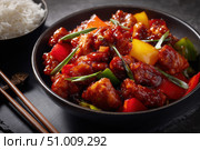 Sweet sour pork with colorful peppers, mixed vegetables served in a black bowl on dark concrete background. Traditional Chinese dish. Close-up. The meat pieces in a brown sauce glaze. Sichuan cuisine. Стоковое AI-изображение, AI-художник Марина Демидюк / Фотобанк Лори