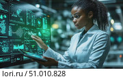 A researcher examines detailed data visualizations on a large screen while holding a tablet, focused on her work in a modern lab environment. Стоковое AI-видео, аниматор Данила Большаков / Фотобанк Лори