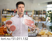 Man in light shirt choose and buy raw cooled beef entrecote and hamburger cutlet in store. Стоковое фото, фотограф Яков Филимонов / Фотобанк Лори