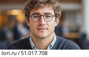 A young man with curly hair and glasses sits in a bustling café, appearing thoughtful and engaged amid lively conversations and a warm ambiance. Стоковое AI-видео, аниматор Данила Большаков / Фотобанк Лори
