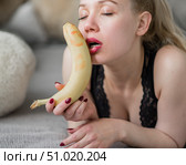 A blonde in black lace lingerie erotically sucks and licks a banana. Unrecognizable woman with sensual red imitates oral pleasure. Стоковое фото, фотограф Михаил Решетников / Фотобанк Лори