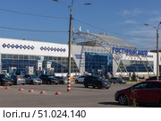 Magnitogorsk, Russian Federation - August 05, 2025: Gostiny Dvor shopping center entrance with modern architecture and blue glass facade, surrounded by trees and parked cars, showcasing urban lifestyle. Редакционное фото, фотограф Ирина Ручушкина / Фотобанк Лори