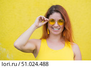 Portrait of a happy woman in sunglasses on a yellow background. Red-haired carefree girl in a dress and earrings tassels of the same color. Lady with an impeccable dazzling smile. Summer photo. Стоковое фото, фотограф Михаил Решетников / Фотобанк Лори