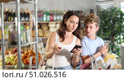 Mom chooses products from a list on her smartphone. Teenage son helps carry shopping cart in a supermarket. Стоковое видео, видеограф Яков Филимонов / Фотобанк Лори