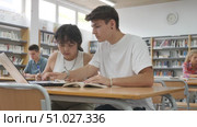 Asian schoolgirl, studying with a classmate guy in the school library on a laptop and making notes in a copybook, preparing for lessons. Стоковое видео, видеограф Яков Филимонов / Фотобанк Лори