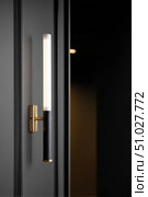 Modern wall lamp illuminating dark room with fluted wall paneling. Стоковое AI-изображение, AI-художник Юрий Поздников / Фотобанк Лори