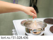 Emale hand dropping raw cleaned squid into boiling water in a metal pot on an electric stove, cooking seafood at home. Стоковое фото, фотограф Татьяна Степанищева / Фотобанк Лори