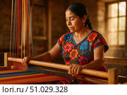 Focused Mexican artisan in a floral embroidered blouse weaving striped fabric on a wooden loom inside a rustic workshop. Стоковое AI-изображение, AI-художник Башкирова Анна / Фотобанк Лори