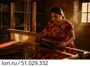 Focused Mexican artisan in embroidered dress operating a large wooden loom to weave traditional striped fabric in warm sunlight. Стоковое AI-изображение, AI-художник Башкирова Анна / Фотобанк Лори