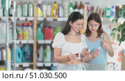 Interested preteen girl with mom in casual summer outfits examining small bottles of brightly colored nail polish during shopping in beauty section of supermarket. Стоковое видео, видеограф Яков Филимонов / Фотобанк Лори