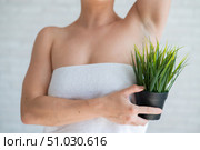 Faceless woman in a white towel holds a pot with a plant. Unrecognizable girl with the help of green bushes imitates the vegetation of armpit hair. Depilation area. Female hair removal. Стоковое фото, фотограф Михаил Решетников / Фотобанк Лори