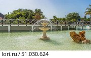 Decorative fountain. Jets of water are sprayed from three tiered bowls. The boulder in the pool. Pedestrian bridge with rope railings over the water. Green tropical vegetation against the sky. Cuba. Стоковое фото, фотограф Вера Ивановна Кубарева / Фотобанк Лори