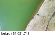 Aerial view of serene green lake with curved shoreline, sandy beach, and gentle waves reflecting sunlight, creating a tranquil natural landscape for relaxation and exploration. Стоковое видео, видеограф Ирина Ручушкина / Фотобанк Лори