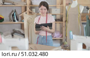 Young female seamstress draws pattern using tablet in sewing workshop. Стоковое видео, видеограф Яков Филимонов / Фотобанк Лори