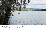 Lake Bannoe, Russian Federation - July 31, 2025: Scenic view of tranquil lake surrounded by lush greenery and distant mountains under a cloudy sky, perfect for nature enthusiasts and outdoor lovers. Редакционное видео, видеограф Ирина Ручушкина / Фотобанк Лори