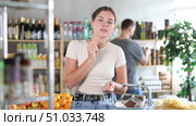 While shopping, girl walks through grocery store, studies windows, looks at assortment of snack. Man takes items from shelf in background, buys groceries, takes them from refrigerator window. Стоковое видео, видеограф Яков Филимонов / Фотобанк Лори