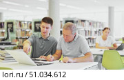Young guy helping older man in laptop interface in public library. Стоковое видео, видеограф Яков Филимонов / Фотобанк Лори