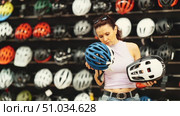 Focused interested female shopper comparing two bicycle helmets, weighing design and safety features, in well-stocked sports store with focus on cycling gear. Стоковое видео, видеограф Яков Филимонов / Фотобанк Лори